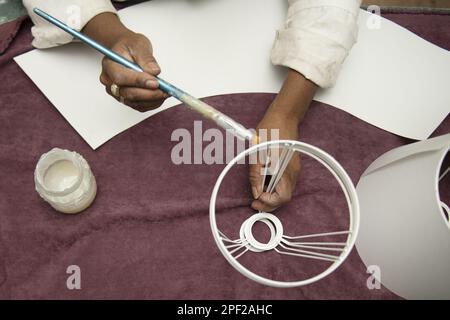 Mani di una donna che applica colla con una lunga spazzola al metallo di un paralume su una tovaglia viola Foto Stock
