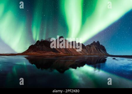 Aurora borealis aurora boreale sulle famose montagne Stokksnes sul capo Vestrahorn. Riflessione nelle acque limpide sullo sfondo dei cieli epici, l'Islanda. Fotografia di paesaggi Foto Stock