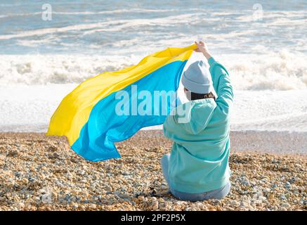 Donna brunnete con cappuccio blu e cappello blu con bandiera nazionale dell'Ucraina, concetto patriottico Foto Stock