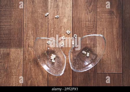 La lastra trasparente è divisa in due parti. Una tazza di zuppa di spaghetti sotto forma di figure per il pranzo cadde sul pavimento di legno e si spezzò. Foto di alta qualità Foto Stock