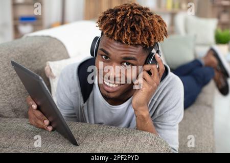 uomo sul divano che usa il tablet e le cuffie Foto Stock