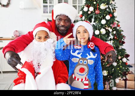 famiglia - papà, figlia e figlio vestito come babbo natale, con una falsa barba e in maglioni di natale con il sorriso delle renne sullo sfondo del natale Foto Stock