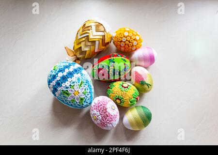 Uova di Pasqua colorate con ornamenti floreali, decorazioni origami e lana di crewel su sfondo bianco, diverse tecniche di decorazione delle uova di Pasqua. Foto Stock