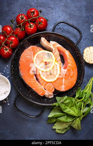 Pesce fresco crudo con verdure pronte per la cottura. Bistecche di salmone crudo con limone, spezie ed erbe aromatiche in padella. Ingredienti per cucinare su un cemento rustico Foto Stock