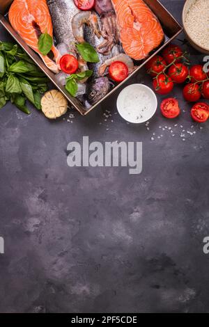 Pesce e frutti di mare assortiti. Bistecca di salmone fresco crudo, trota, calamari, gamberetti con verdure e riso pronto per la cottura. Ingredienti per cucinare su calcestruzzo Foto Stock