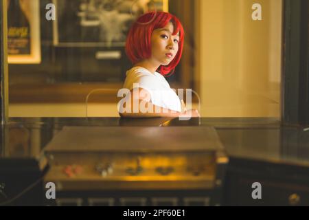 Ragazza adolescente in Wig rosso brillante in piedi presso la biglietteria del film vecchio stile Foto Stock