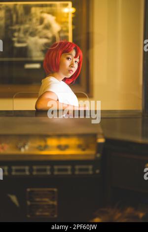 Ragazza adolescente in Wig rosso brillante in piedi presso la biglietteria del film vecchio stile Foto Stock