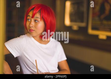 Ragazza adolescente in Wig rosso brillante in piedi presso la biglietteria del film vecchio stile Foto Stock