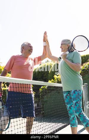 Felice caucasico anziani amici in alto fiving a campo da tennis il giorno di sole, copia spazio Foto Stock