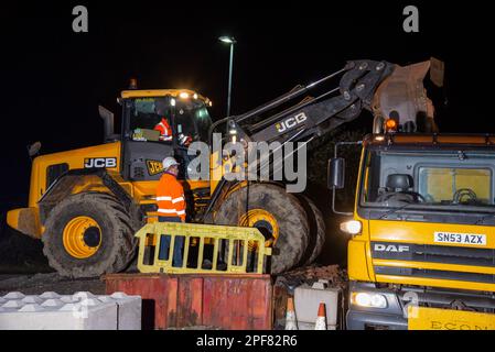 Un veicolo DAF gritter viene caricato di notte da un digger JCB a Denby Dale, West Yorkshire Foto Stock