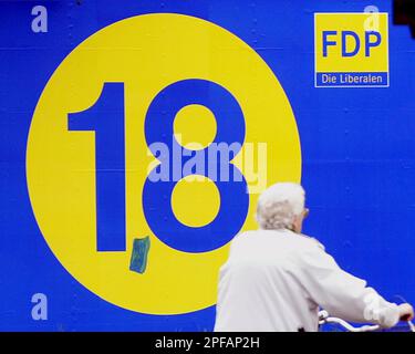 An elderly woman pushes her bicycle past an election poster of the German Liberal Democratic Party (FDP) in Duisburg, western Germany, Saturday, Sept. 21, 2002, one day ahead of the general elections in Germany on Sunday, Sept. 22nd. The big 18 refers to the party's aim to win 18 percent of the votes as an unidentified person had painted a decimal point between the one and eight. (AP Photo/Frank Augstein)