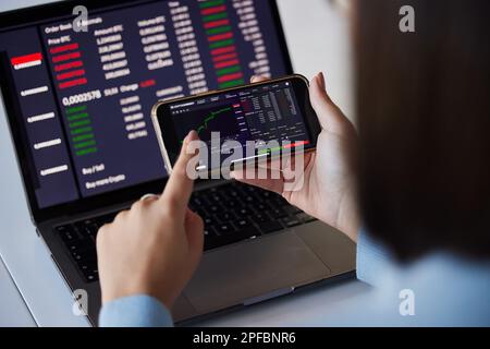 Grafico di borsa, portatile e telefono in mano di donna per cripto, analisi dei dati e schermo bitcoin. FinTech crescita, e-commerce e ragazza sulla tecnologia Foto Stock