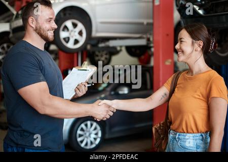 Bene faccia la vostra automobile funzionare uniformemente ancora. una donna che scuote le mani con un meccanico in un negozio di riparazione auto. Foto Stock