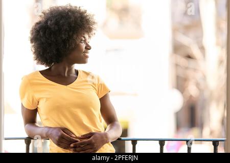 Distratta donna africana appoggiata sulla rotaia di una terrazza Foto Stock