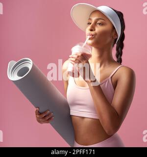 Rimani in forma, non preoccuparti di entrare. una giovane donna attraente e sportiva che si posa con un tappetino per esercizi e un frullato in studio contro un rosa Foto Stock