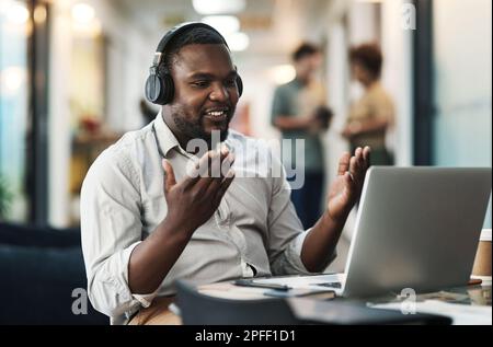Abbiamo tanti piani per l'anno a venire. un giovane uomo d'affari seduto in ufficio e indossando le cuffie mentre usa il suo computer portatile per un virtuale Foto Stock