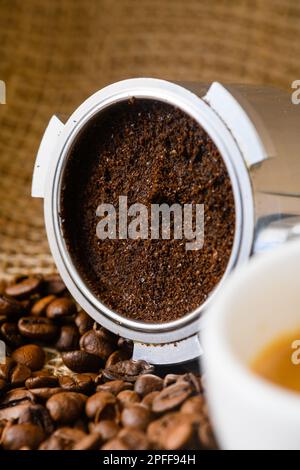 Caffè macinato o usato con portafiltro e una tazza di caffè appena preparato sullo sfondo Foto Stock