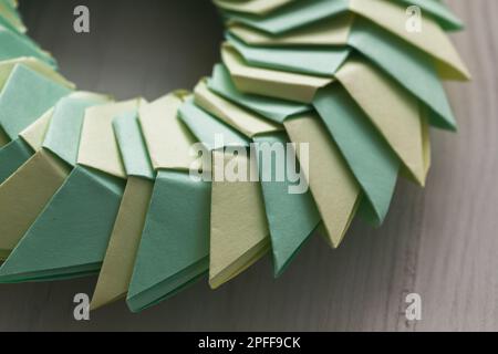 L'anello Origami, struttura circolare parametrica astratta realizzata in fogli di carta verde e giallo, è adagiato su una scrivania bianca Foto Stock
