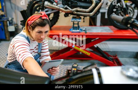 Meccanico femminile concentrato con tablet digitale che rivede le informazioni della moto in garage Foto Stock