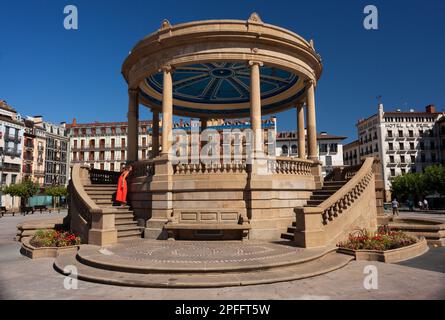 Pamplona, Spagna - 2 agosto 2022: Donna che indossa un abito rosso accanto al monumento Padiglione in Piazza del castello nella città vecchia di Pamplona Spagna. Foto Stock