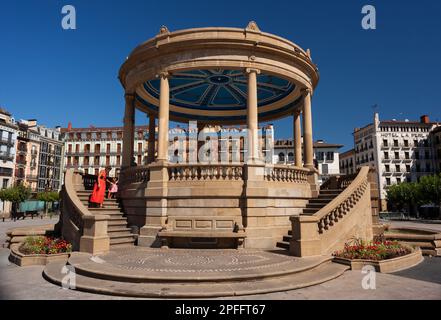 Pamplona, Spagna - 2 agosto 2022: Donna che indossa un abito rosso con la figlia accanto al monumento Padiglione in Piazza del castello nella città vecchia di Foto Stock