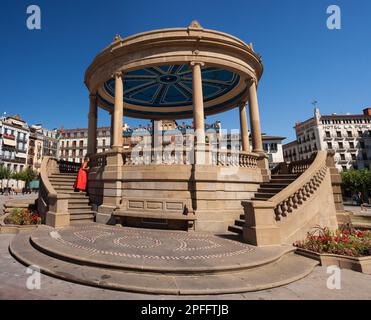 Pamplona, Spagna - 2 agosto 2022: Donna che indossa un abito rosso accanto al monumento Padiglione in Piazza del castello nella città vecchia di Pamplona Spagna. Foto Stock