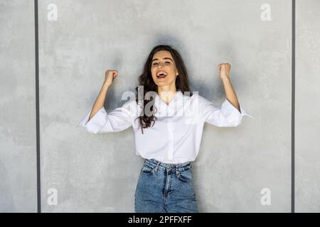 Donna felice esulta pugni di pompaggio entusiasta celebra il successo isolato sul muro grigio sfondo Foto Stock