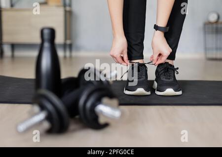 concetto di sport e stile di vita sano - donna che si prepara per l'allenamento a casa e le scarpe da ginnastica - manubri neri e bottiglia d'acqua in fi Foto Stock