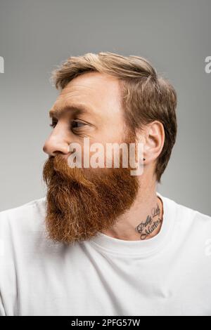 Ritratto di uomo tatuato in t-shirt guardando lontano isolato su grigio, immagine stock Foto Stock