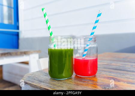 Due barattoli di mason riempiti di succo rosso e verde appena sfornato, completi di cannucce colorate, posti su un tavolo di legno in una caffetteria biologica. Foto Stock