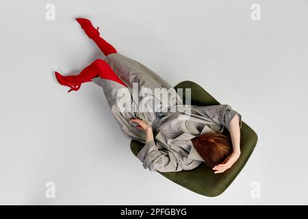 Emozioni umane impersonali. Elegante ragazza con cappotto grigio e collant rosso brillante si muove su sfondo chiaro. Moda espressiva. Concetto di fotografia d'arte Foto Stock