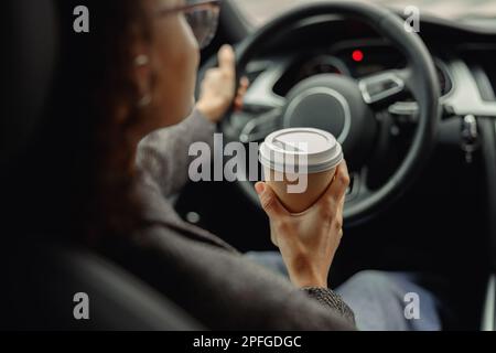 Primo piano di una giovane donna che beve caffè da togliere durante la guida per lavorare in auto Foto Stock