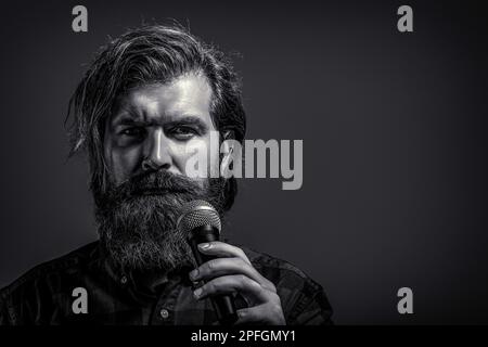 Uomo bearato che canta con il microfono. Maschio che canta con un microfono. Uomo con barba che tiene un microfono e canta. Bianco e nero Foto Stock