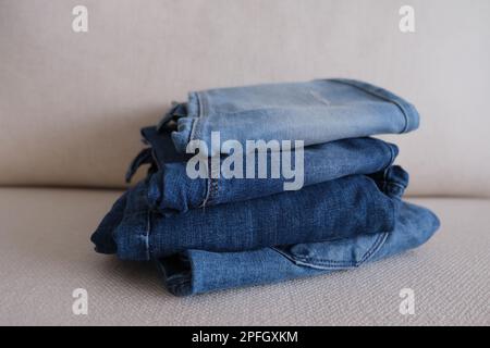 Pantaloni in denim, quattro pantaloni in denim ripiegati e impilati su un divano bianco, foto idea in tessuto denim. Foto Stock
