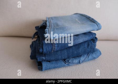 Quattro pantaloni denim, pantaloni denim ripiegati e impilati su un divano bianco, foto idea in tessuto denim. Foto Stock