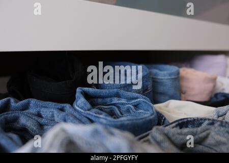 Cassettiera piena di pantaloni in denim, cassettiera aperta con pantaloni jeans in denim ripiegati e arrotolati in interni, primo piano. Pantaloni arrotolati concept foto. Foto Stock