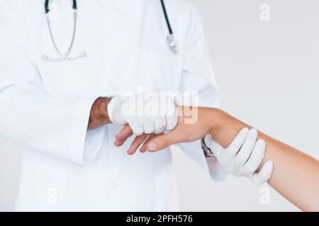 Medic lavora con la mano del paziente. Vista ravvicinata delle particelle di un giovane uomo che si erge all'interno su sfondo bianco Foto Stock