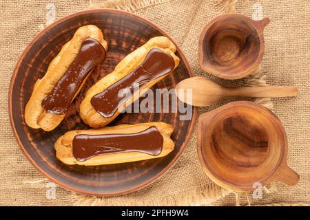 Tre ciotole di cioccolato con un piatto di argilla e due tazze di legno su un panno di iuta, primo piano, vista dall'alto. Foto Stock