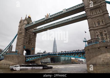 Vista del tour in barca turistico e del Tower Bridge dalla gita in barca sul livello dell'acqua. Attraversa il Tamigi tra Southwark e la City of London, Regno Unito. Il grattacielo Shard è visibile attraverso l'apertura. (133) Foto Stock