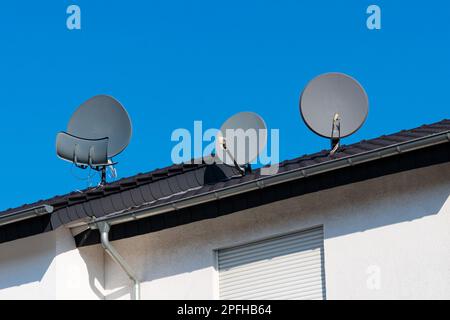 Tre piatti satellitari sul tetto di una casa piastrellata. Cielo blu chiaro. Foto Stock