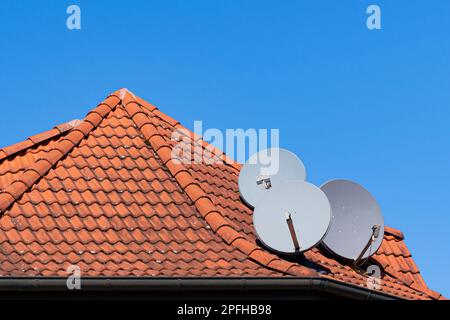 Tre parabole grigie sul tetto di una casa piastrellata. Cielo blu chiaro. Foto Stock