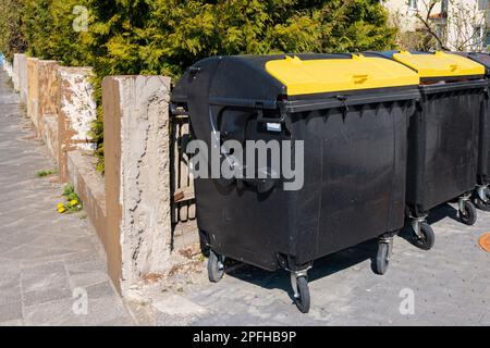 Due bidoni di rifiuti con coperchi gialli sono accatastati in una fila lungo il muro di cemento. Foto Stock