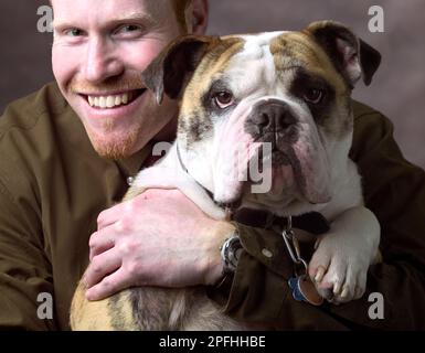 Un ritratto di giovane uomo con il suo cane da compagnia su uno sfondo piano Foto Stock