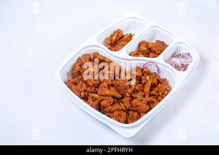 Fritto Gobi Manchurian secco con cipolle affettate in scatola di plastica su sfondo bianco, popolare spuntino indiano sera, Foto Stock