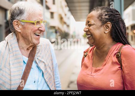 Felici amici anziani multirazziali che parlano mentre aspettano alla stazione degli autobus Foto Stock