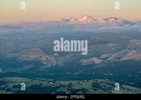 Vista aerea della valle e delle montagne della catena montuosa della Cantabria con alcune fitte nuvole arroccate su di essa in un tramonto visto da Peña Cabarga, Foto Stock