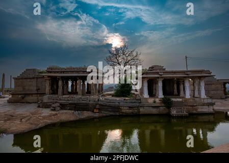 Rovine su vecchi templi oltre a uno stagno sulla collina di Hemakuta in Hampi. Hampi, la capitale dell'impero Vijayanagar, è un sito patrimonio dell'umanità dell'UNESCO. Foto Stock