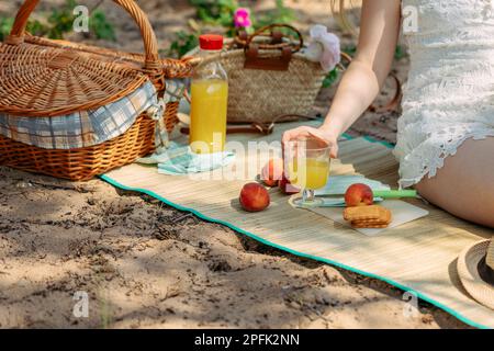 Picnic estivo sulla spiaggia via mare. Frutta fresca, succo di frutta, biscotti e pesche vicino al cestino da picnic su un panno. Foto di alta qualità Foto Stock