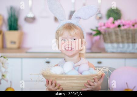 La bambina tiene un cestino con uova di Pasqua dipinte. Bambino felice nella cucina luminosa a casa il giorno di Pasqua. Foto Stock