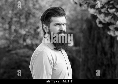 Uomo ispanico di successo in giardino di primavera. Ritratto di un giovane uomo bello, modello di moda, con acconciatura formale pensiero in primavera parco, vestendo Foto Stock